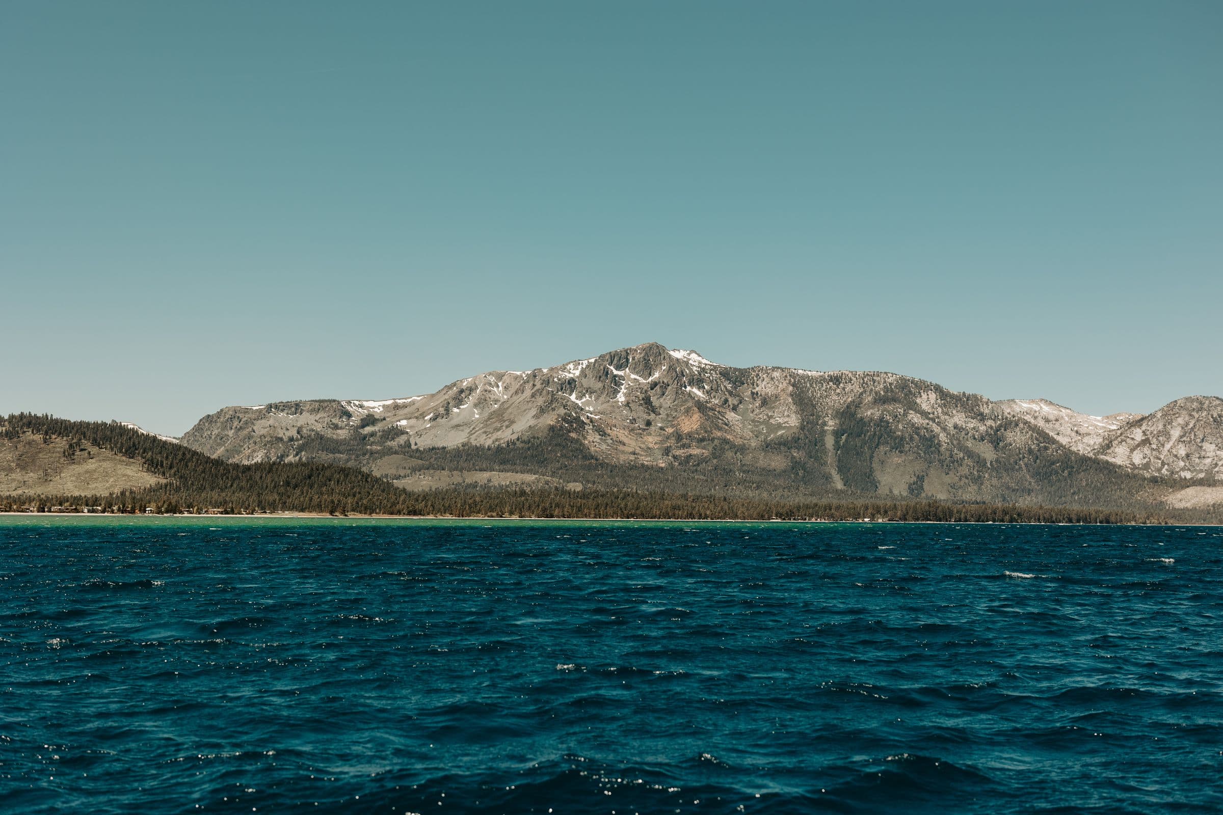 Snow-dusted Sierra Nevada peaks rising beyond the deep blue water of Lake Tahoe